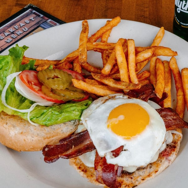 Mamas Kitchen breakfast sandwich with bacon, fried egg, lettuce, tomato, onion, pickles, and fries.