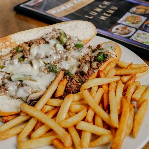 Cheesesteak sandwich with melted cheese, peppers, and onions, served with a side of golden fries.