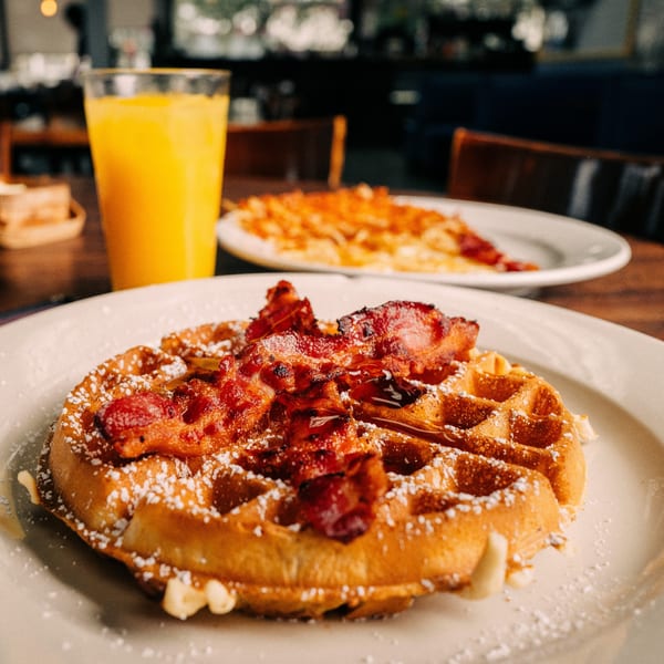 Mamas Kitchen waffle with bacon, powdered sugar, and syrup, with orange juice and hash browns.